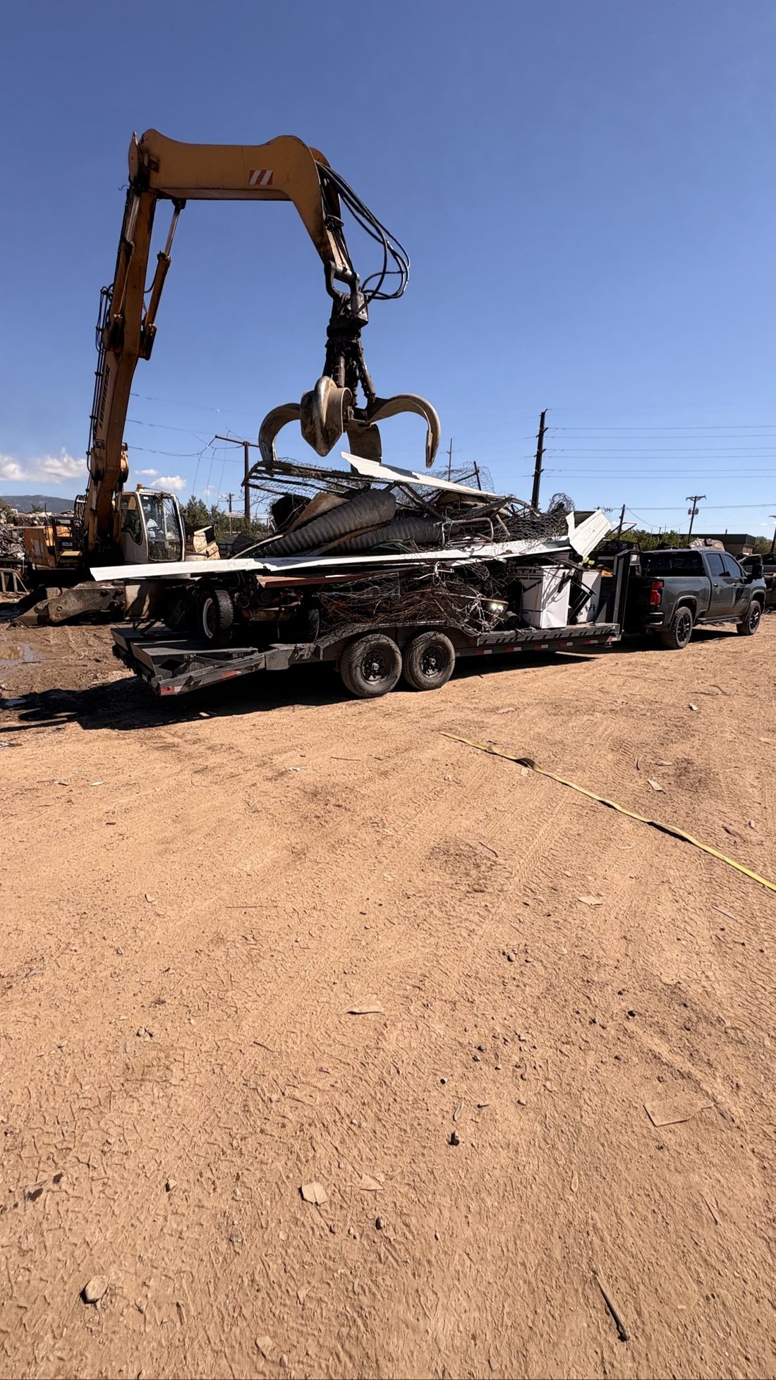 Excavator grapple loading scrap and debris onto a BK Hauling trailer