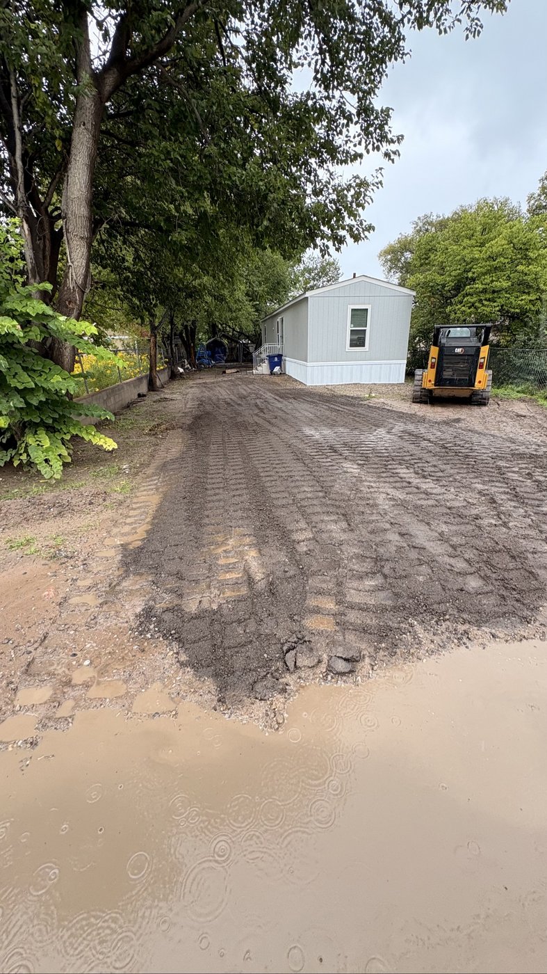 Same lot after — freshly graded millings driveway with the CAT skid steer parked beside the house