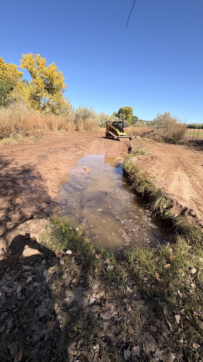 Same drainage ditch after BK Hauling & Clearing graded the banks smooth, CAT skid steer parked at the far end
